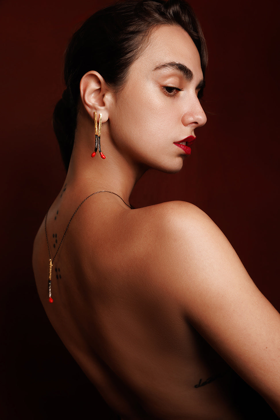 Model wearing matchstick earrings and matchstick necklace against a dark red backdrop