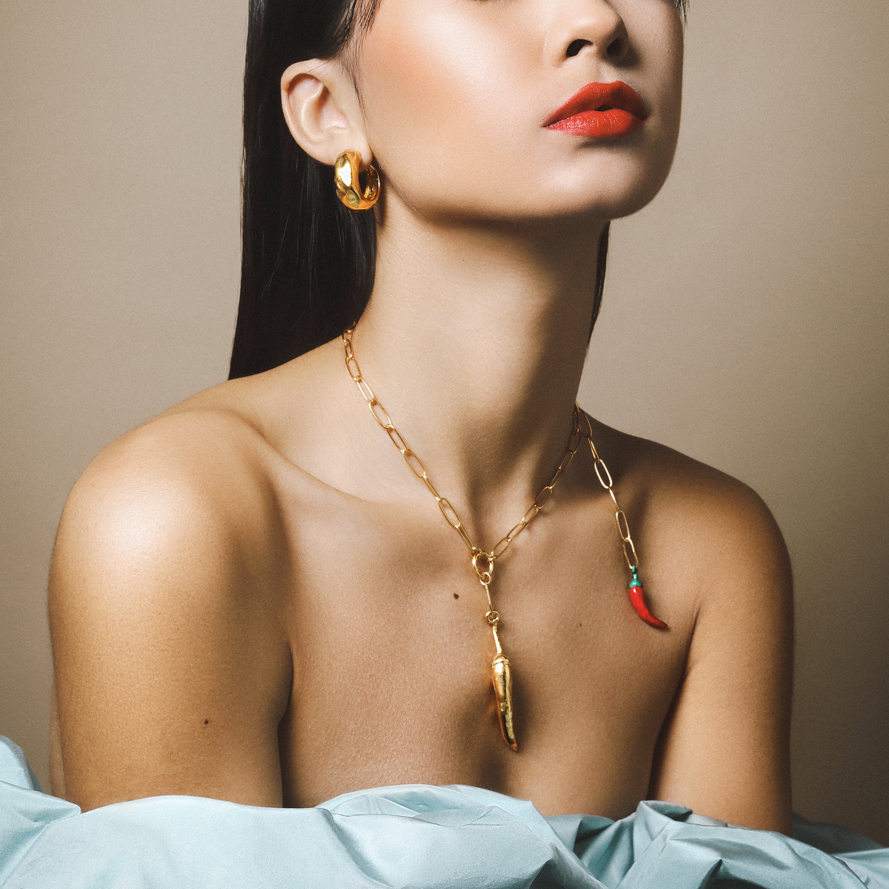 Set of gold chili inspired jewellery worn by an almost topless model against a beige backdrop